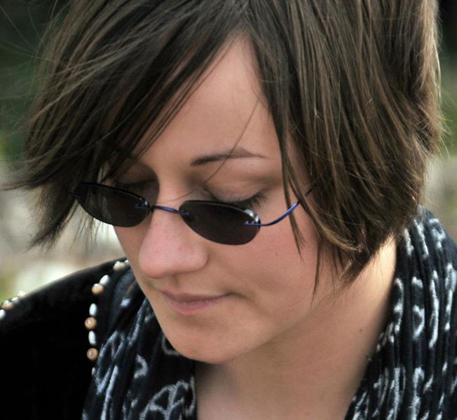 A photo of a woman wearing sunglass and a scarf with peace signs on it, looking down.